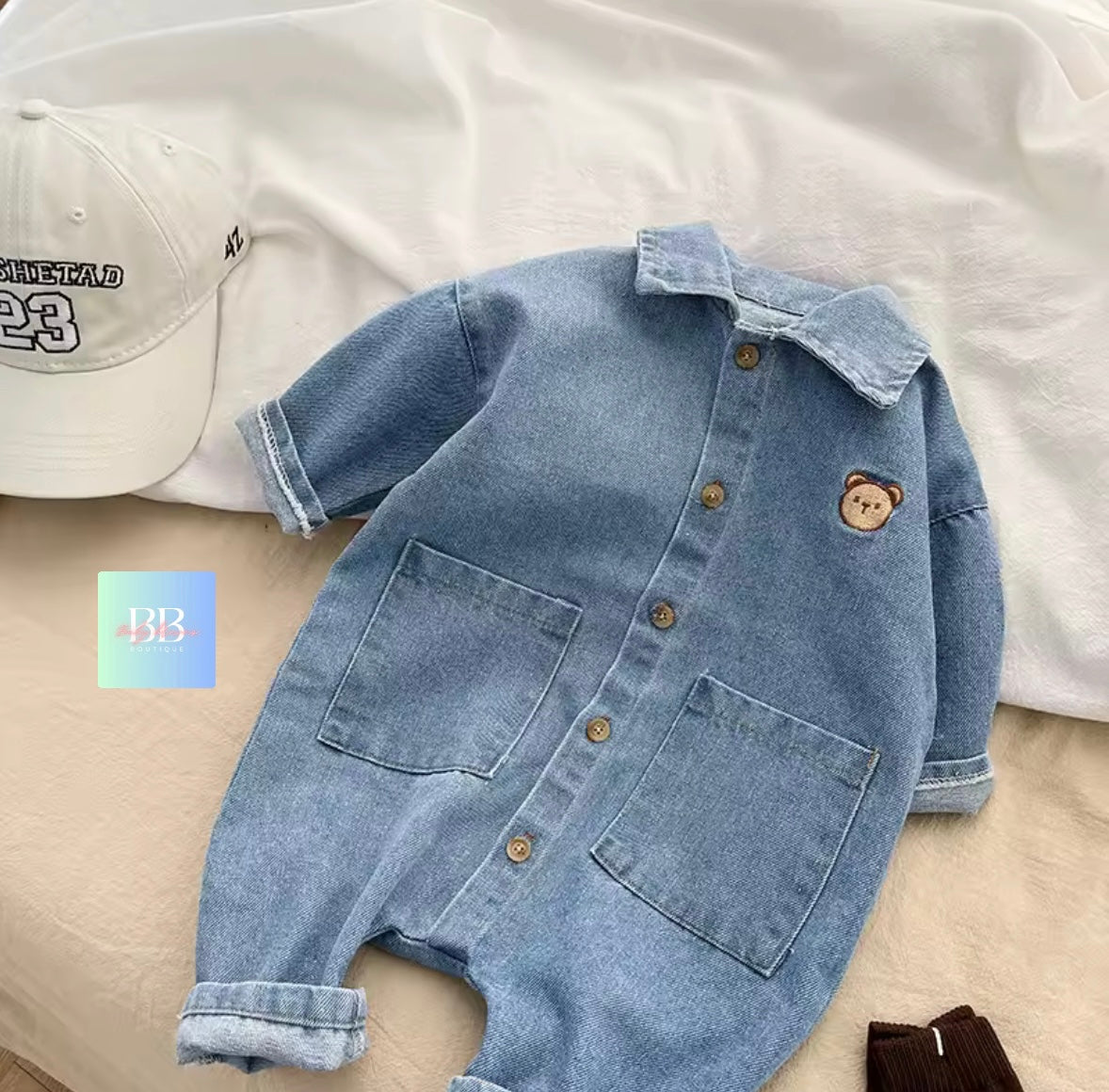 Light blue denim romper with bear patch on a white background
