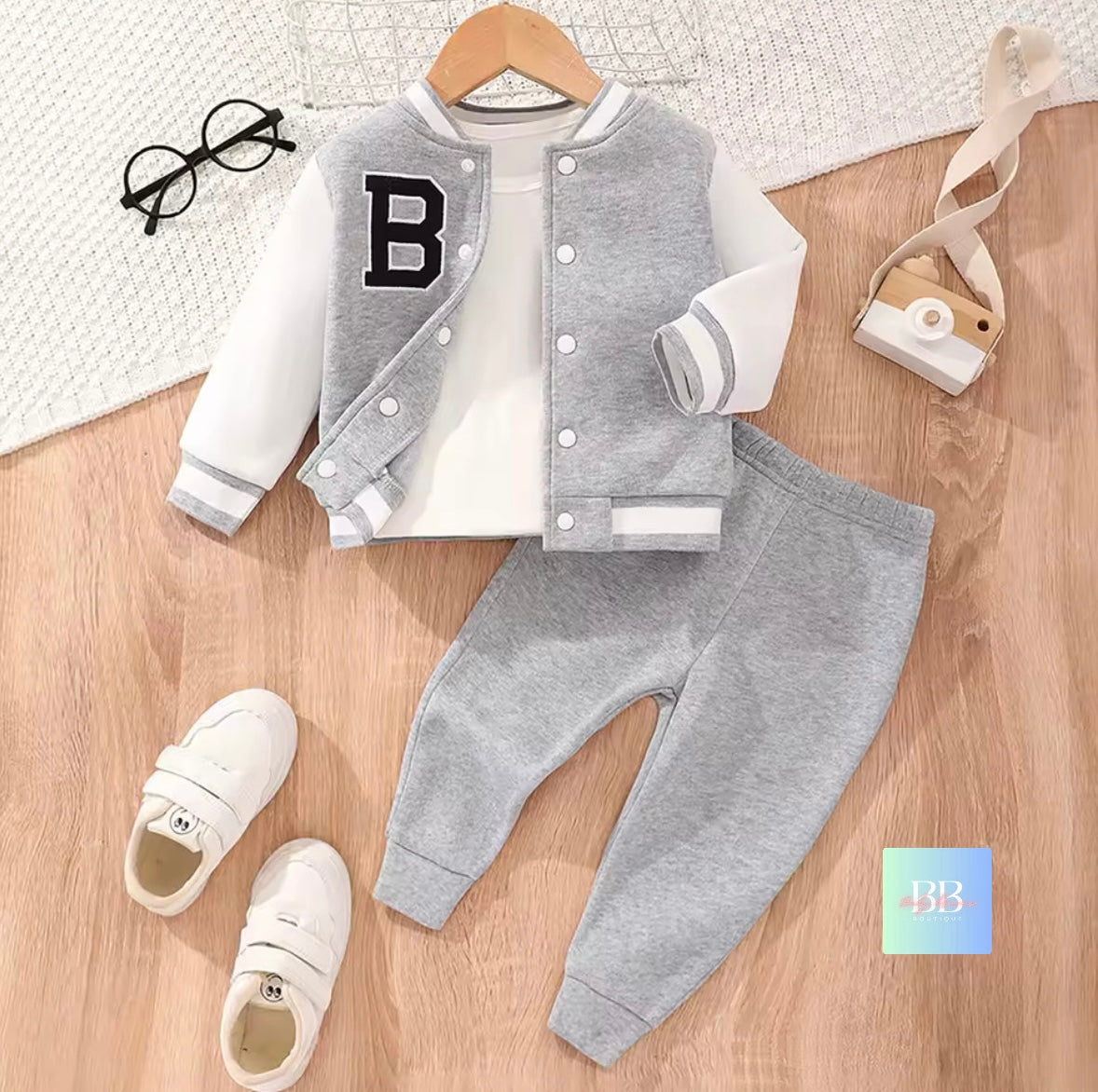 Children's gray varsity jacket with letter 'B', white shirt, gray pants, and white sneakers on a wooden surface.