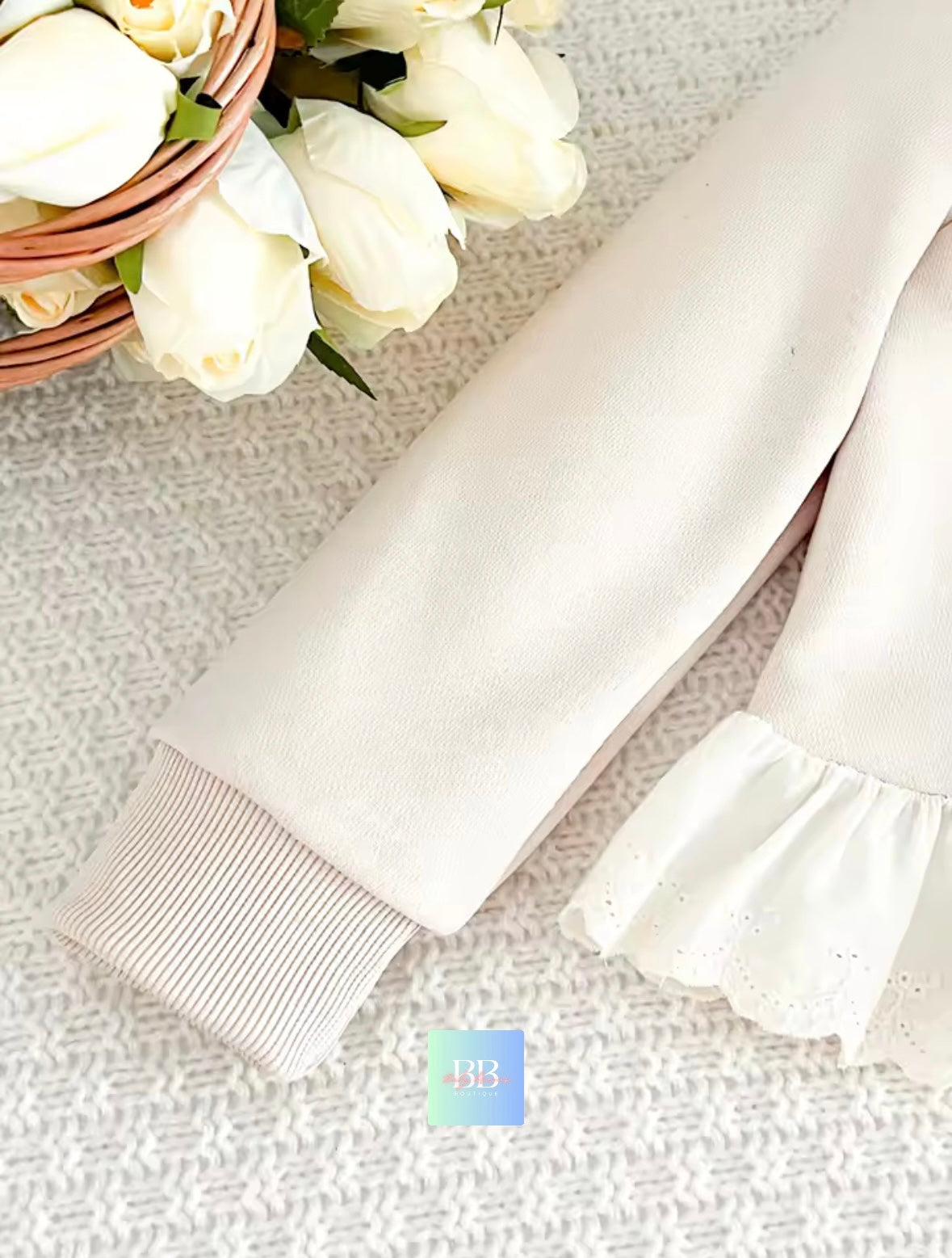 White baby pants with ruffled details on a textured surface with flowers in the background