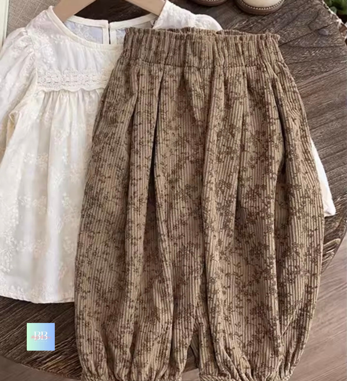 Brown corduroy pants on a wooden surface with a white blouse in the background.