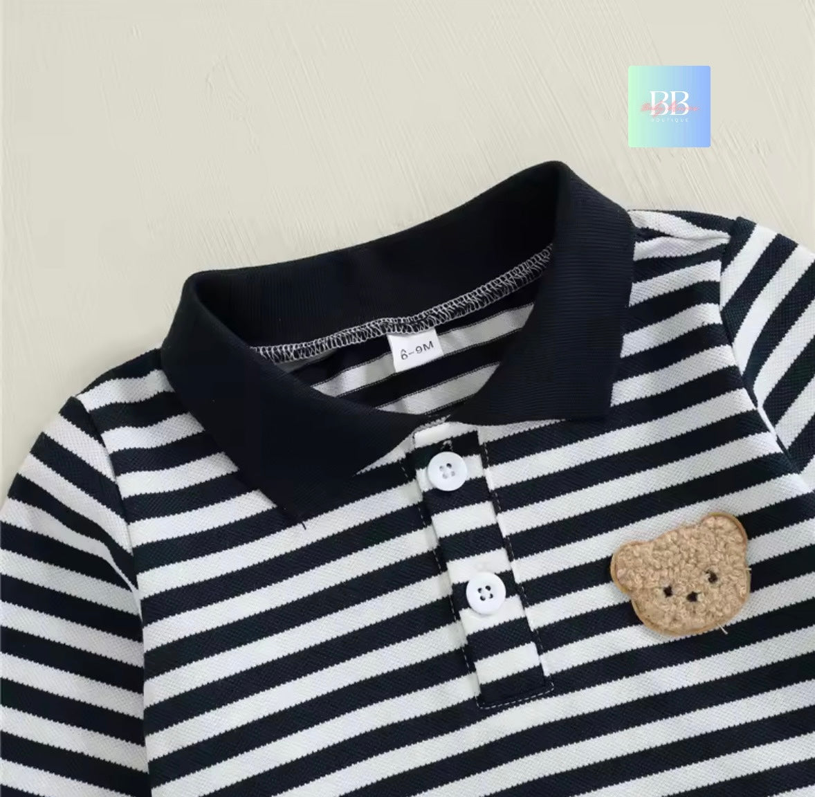 Black and white striped polo shirt with a teddy bear patch on a beige background