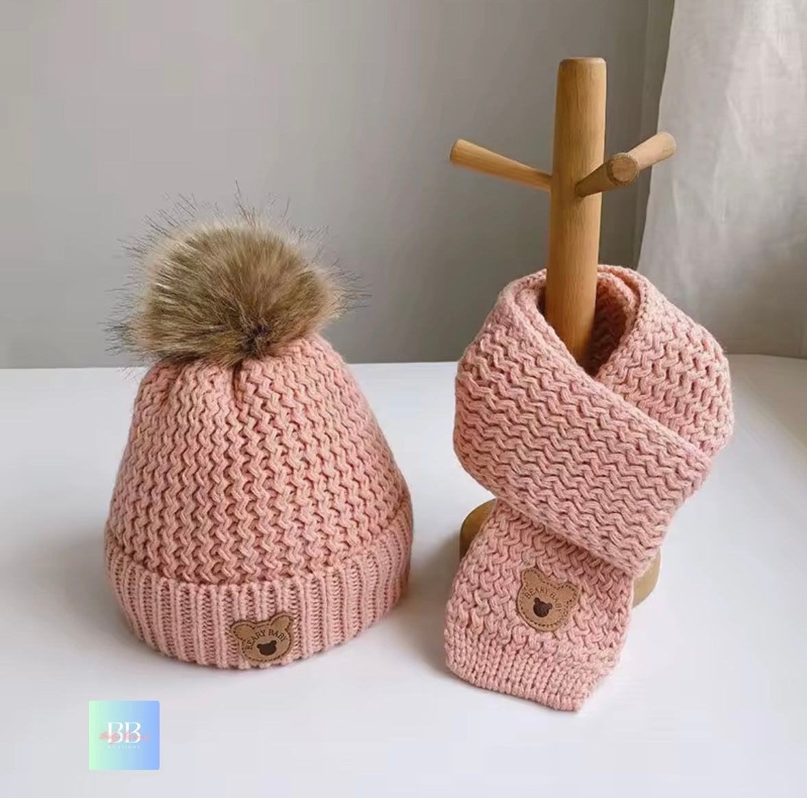 Pink knitted hat and scarf set with a wooden stand on a white surface.