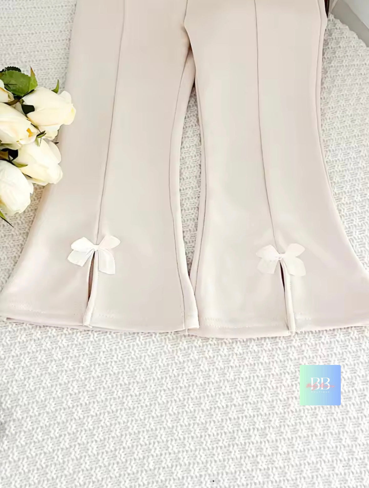 Light gray pants with white bows on a textured surface with flowers.