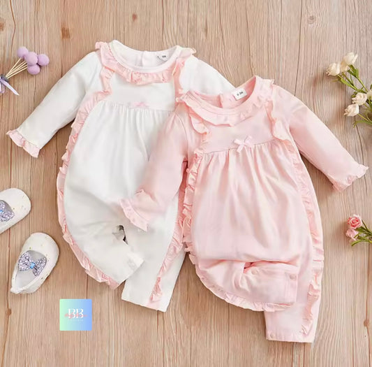 Two baby rompers with ruffled details on a wooden surface.