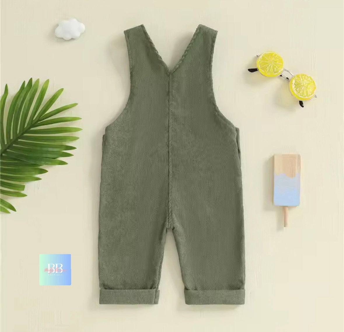 Green denim overalls on a light beige background with decorative items.