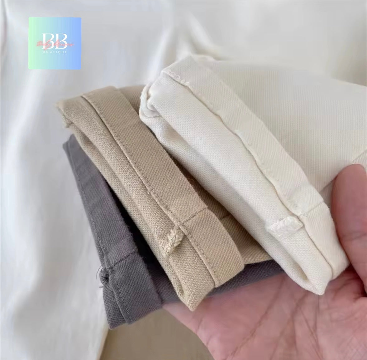 Three pairs of folded tights in beige, gray, and white held in a hand against a white background.