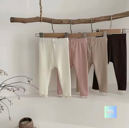 Three pairs of leggings in white, pink, and black hanging on a wooden branch against a white wall.