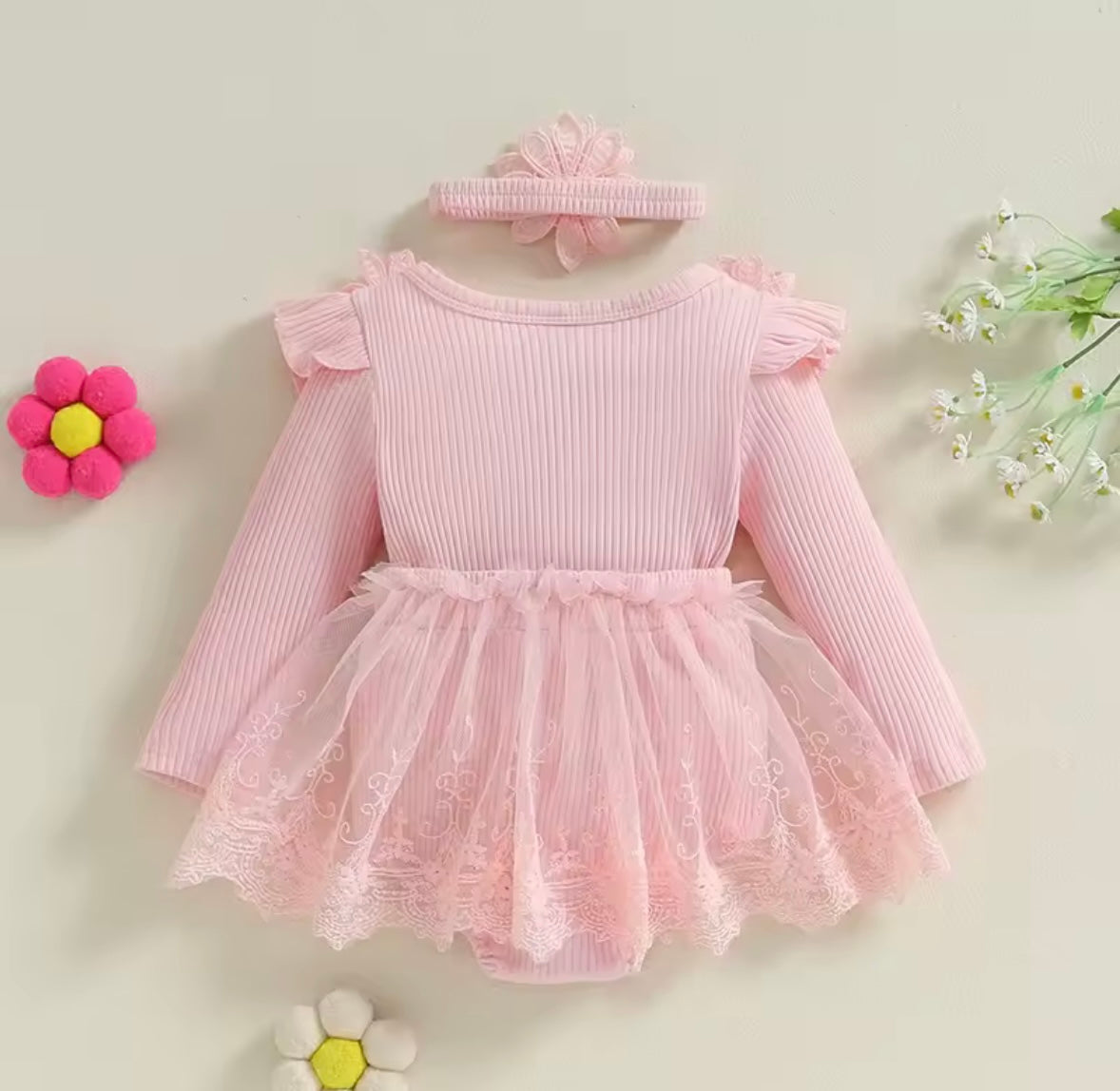 Pink baby dress with ruffles and a matching headband on a light background