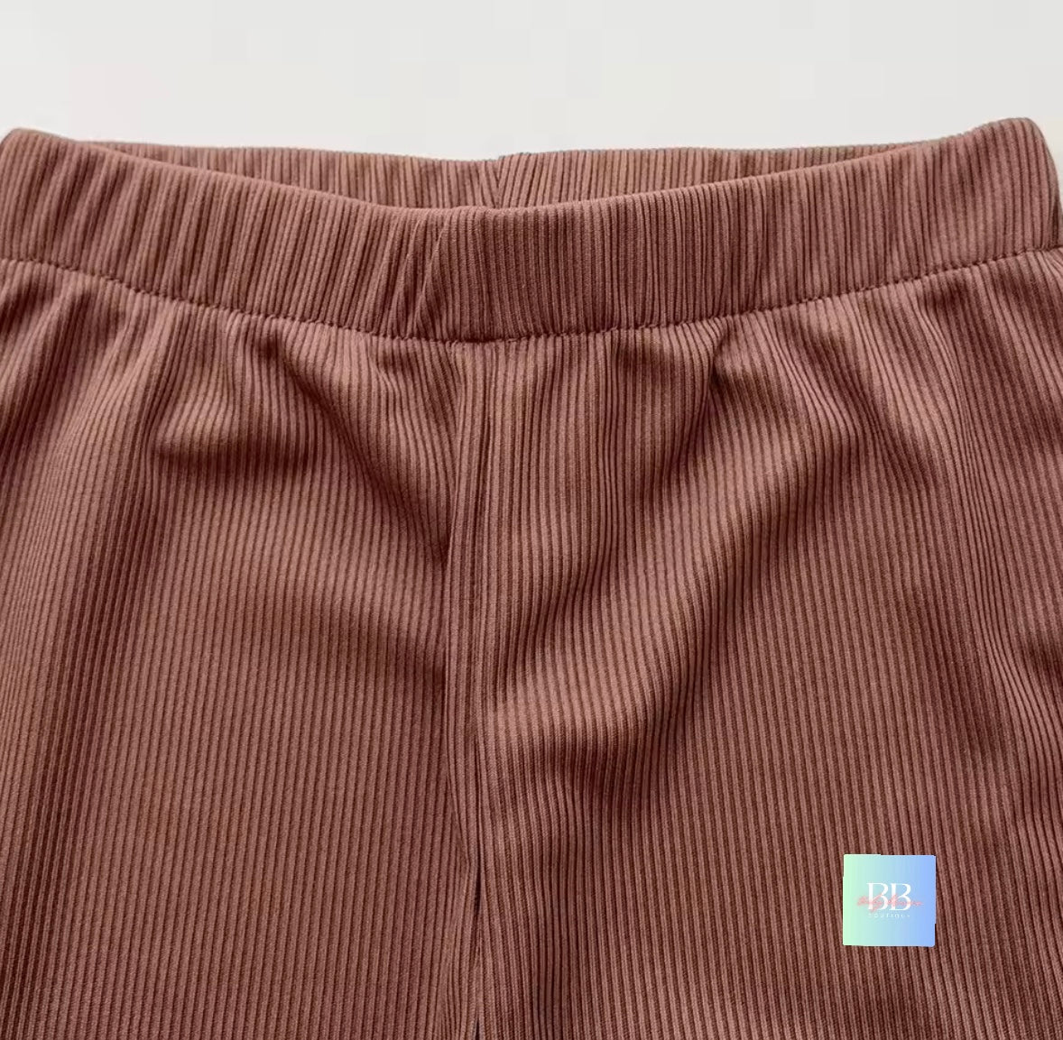 Brown corduroy pants with a small colorful label on a light gray background