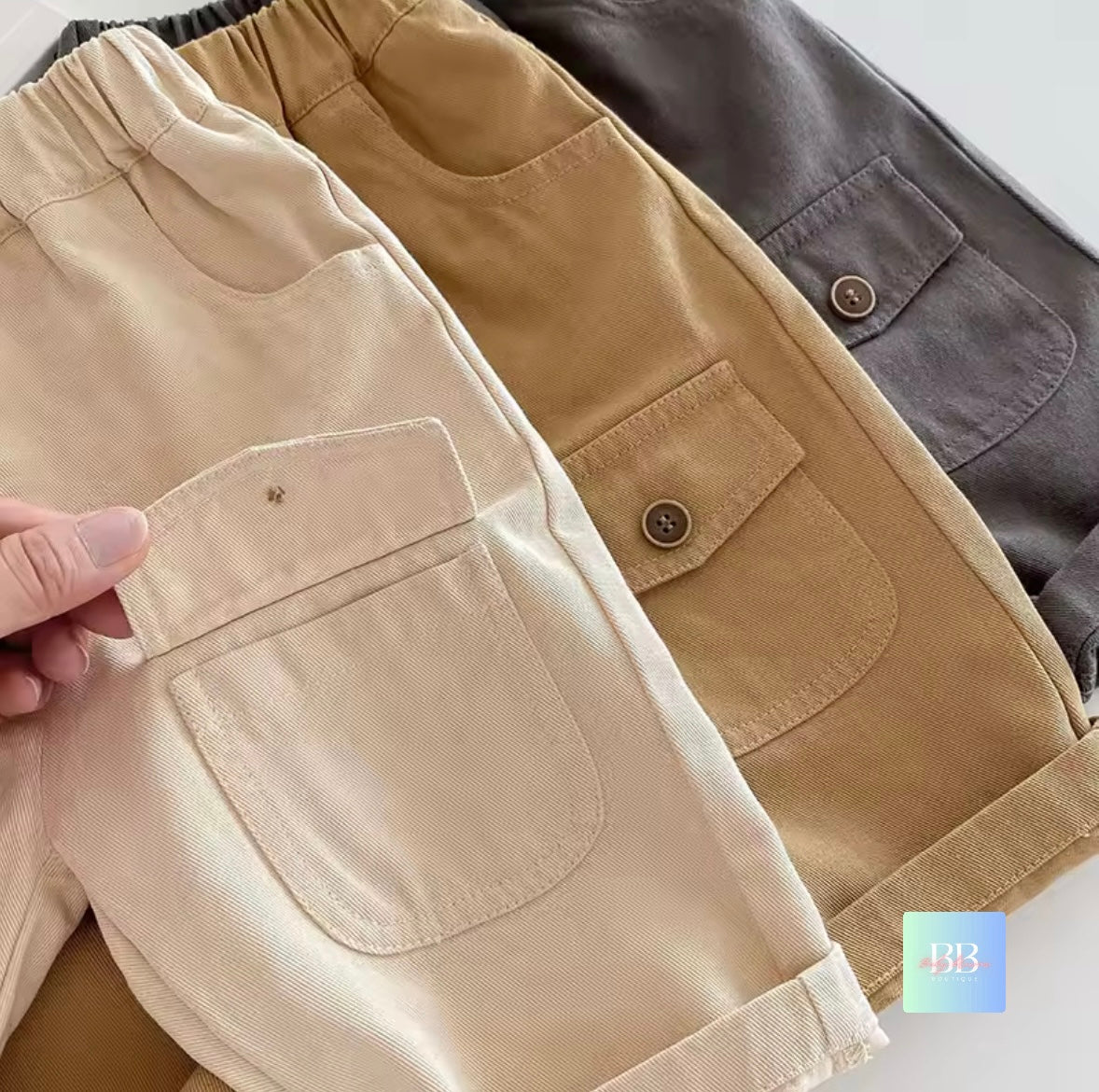 Three pairs of pants in beige, brown, and gray on a white background.