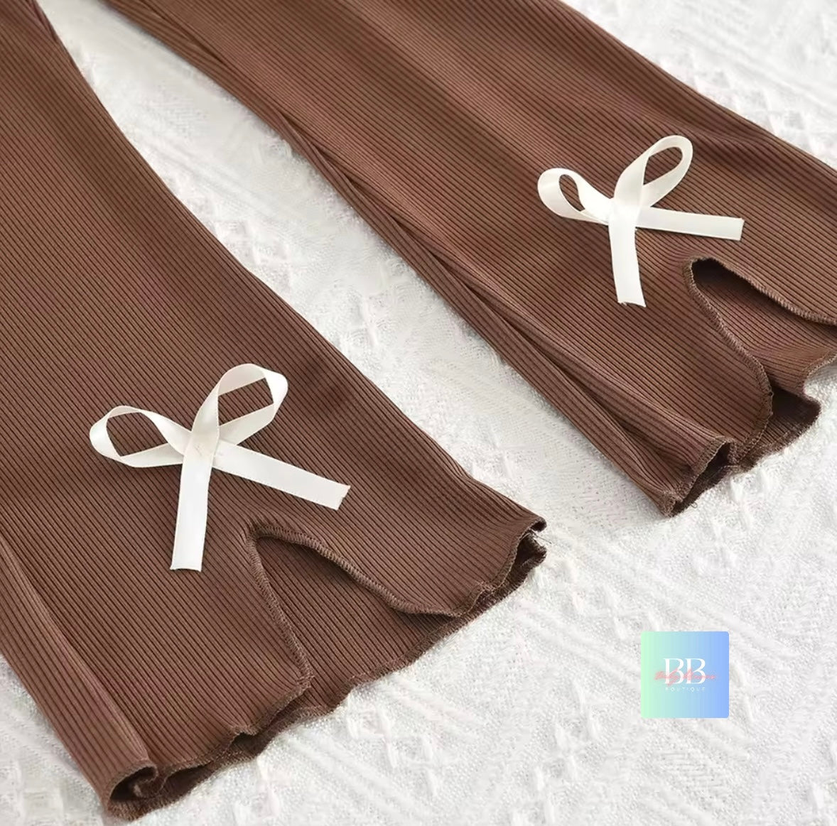 Brown ribbed leggings with white bows on a textured white surface
