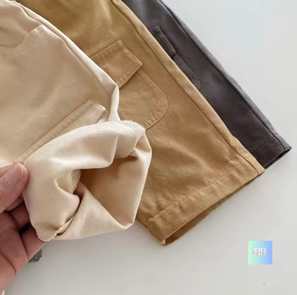Close-up of beige pants with a hand holding a piece of fabric on a light background