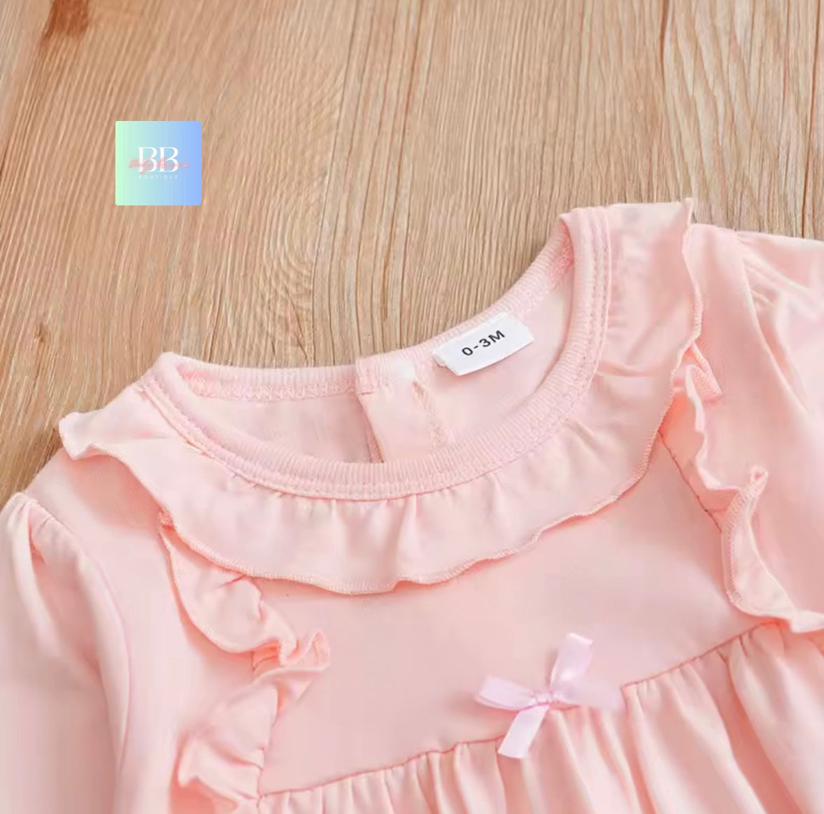 Close-up of a pink baby dress with ruffled collar and bow details on a wooden surface.