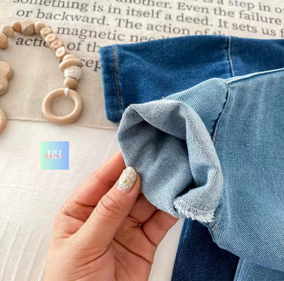 Close-up of a hand holding blue denim fabric with a wooden ring and beads on a textured surface.
