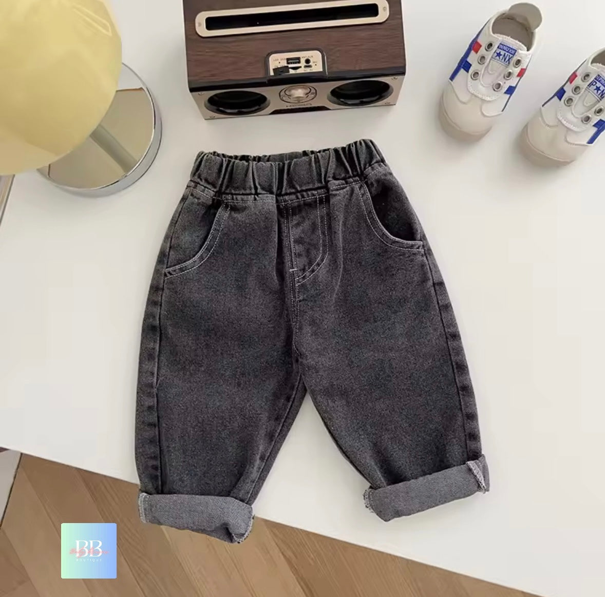 Gray denim pants on a white surface with a small radio and shoes in the background.