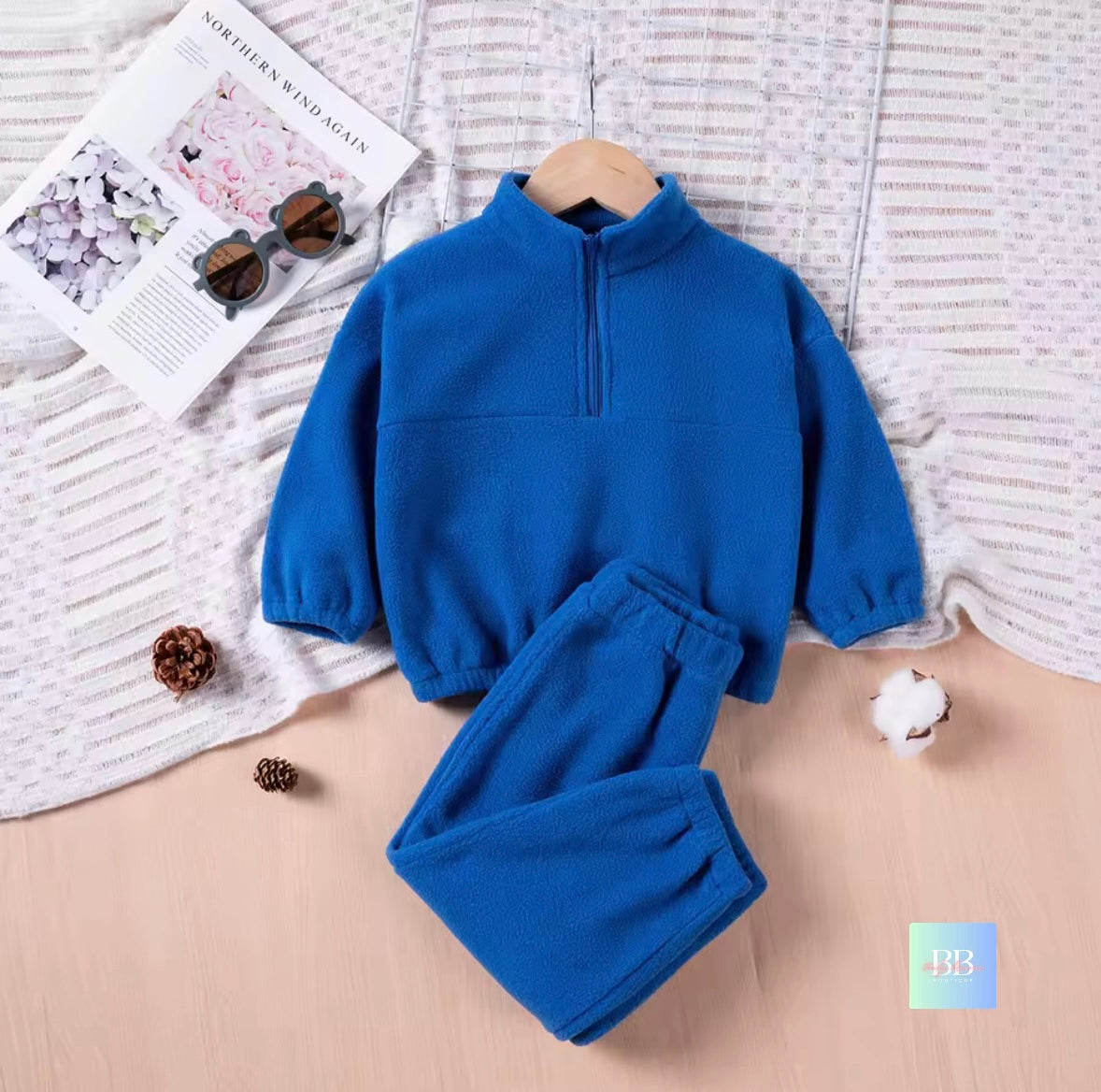 Blue children's fleece set on a textured surface with a magazine and pine cones.
