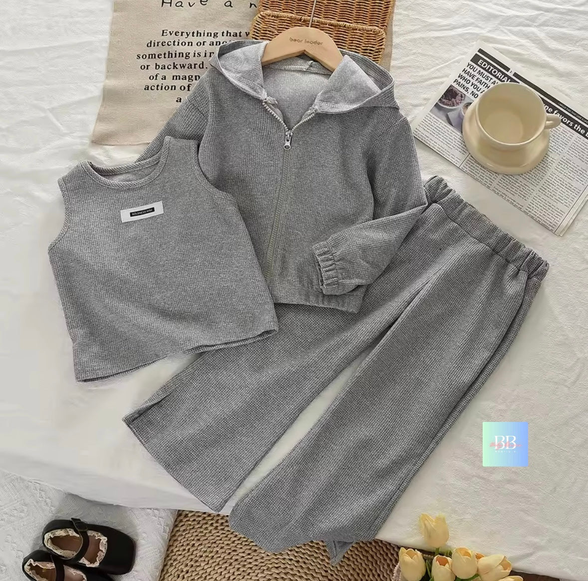 Gray children's outfit with vest, jacket, and pants on a white surface with newspaper and cup.
