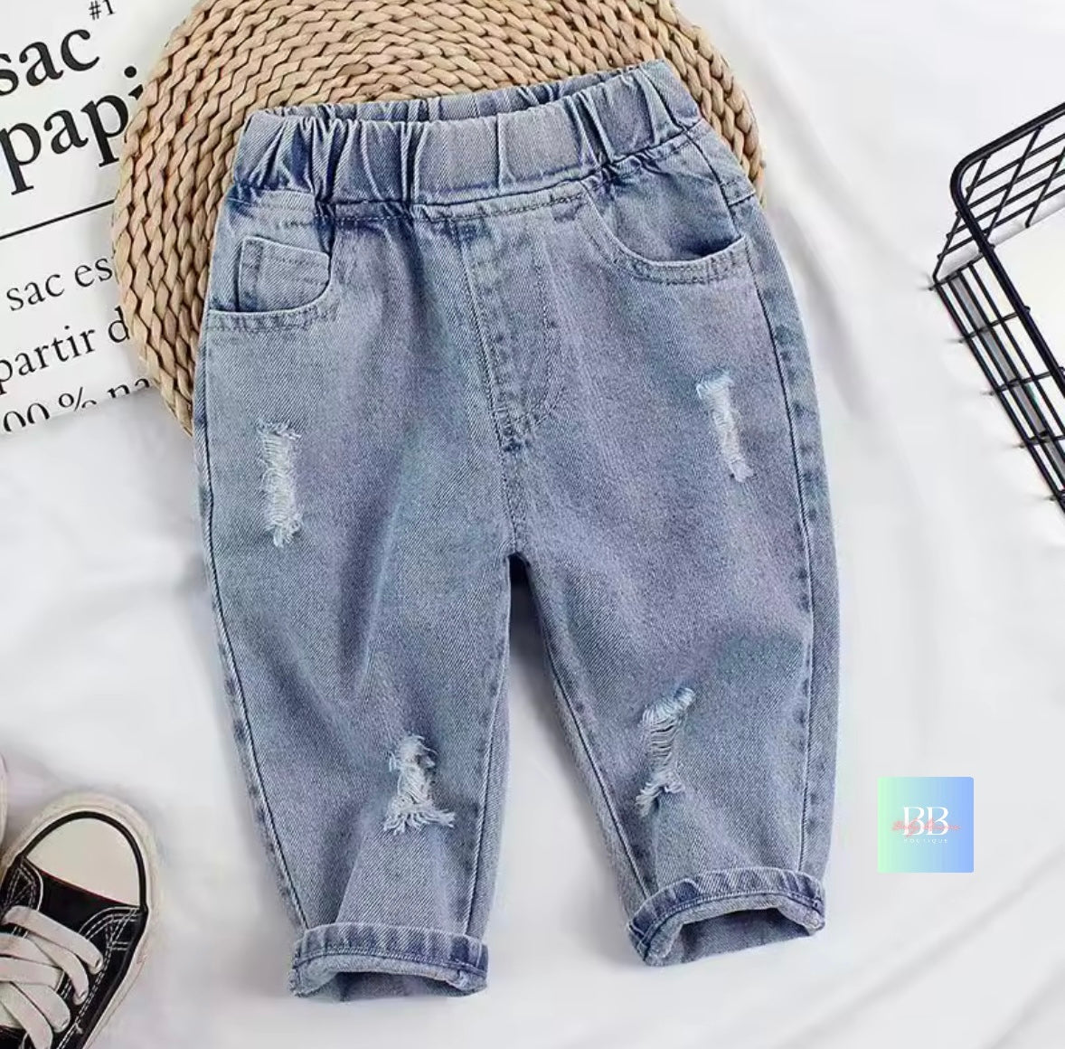Light blue distressed jeans on a white background with a woven mat and black shoes.