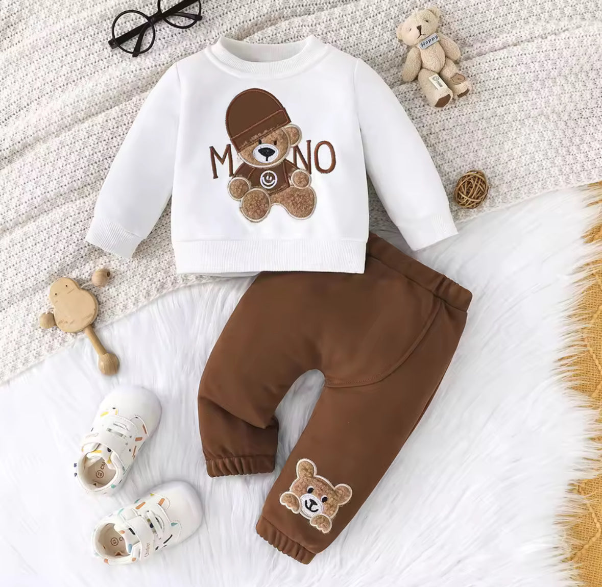 Children's outfit with white shirt and brown pants featuring teddy bear designs on a textured surface.