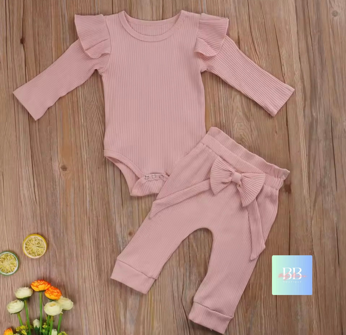 Pink baby outfit with ruffled sleeves and bow details on a wooden surface.