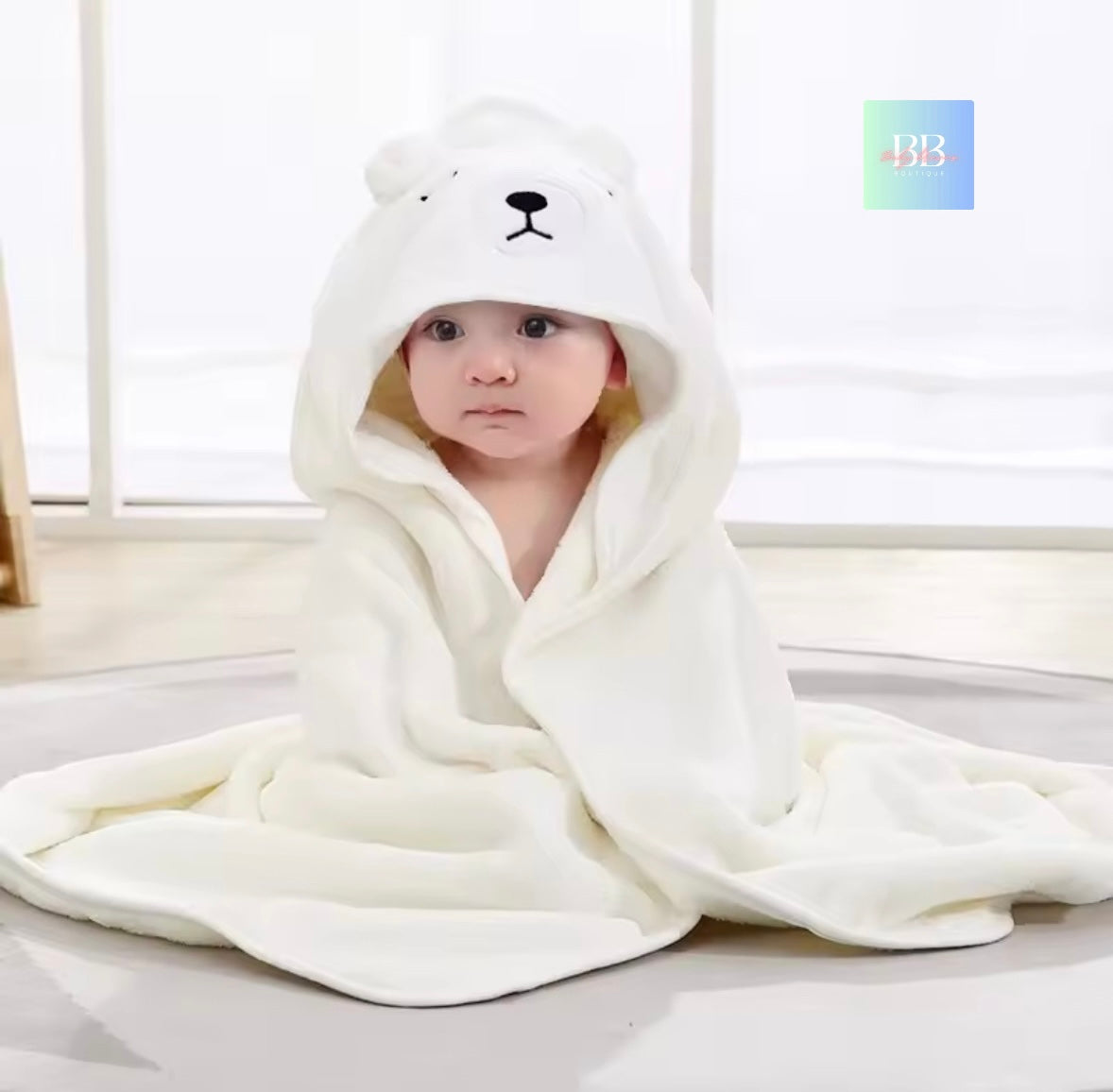 Child wrapped in a white hooded blanket with bear ears and a face, sitting on a light-colored floor.
