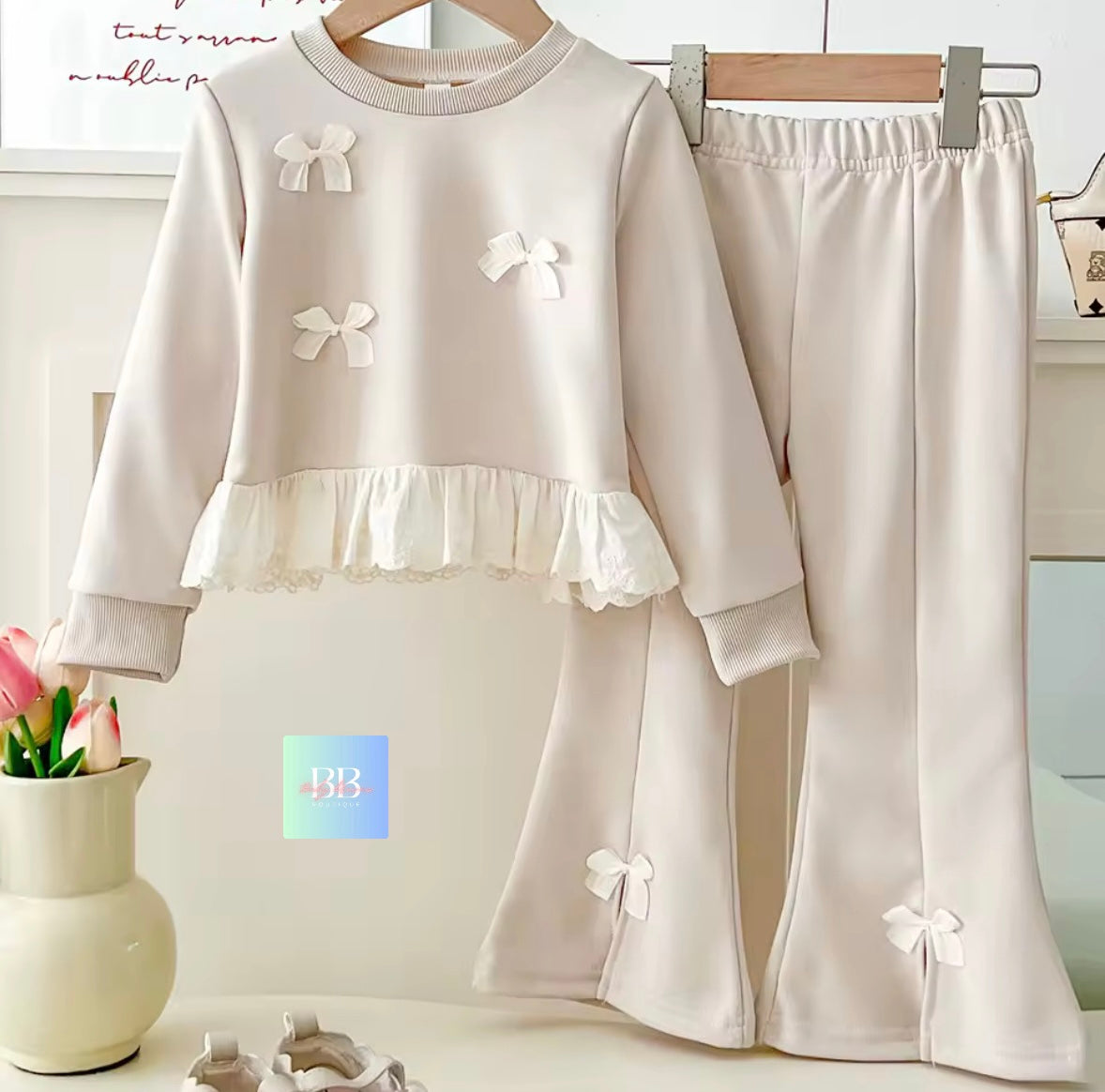 Children's white outfit with bow details on a hanger against a light background