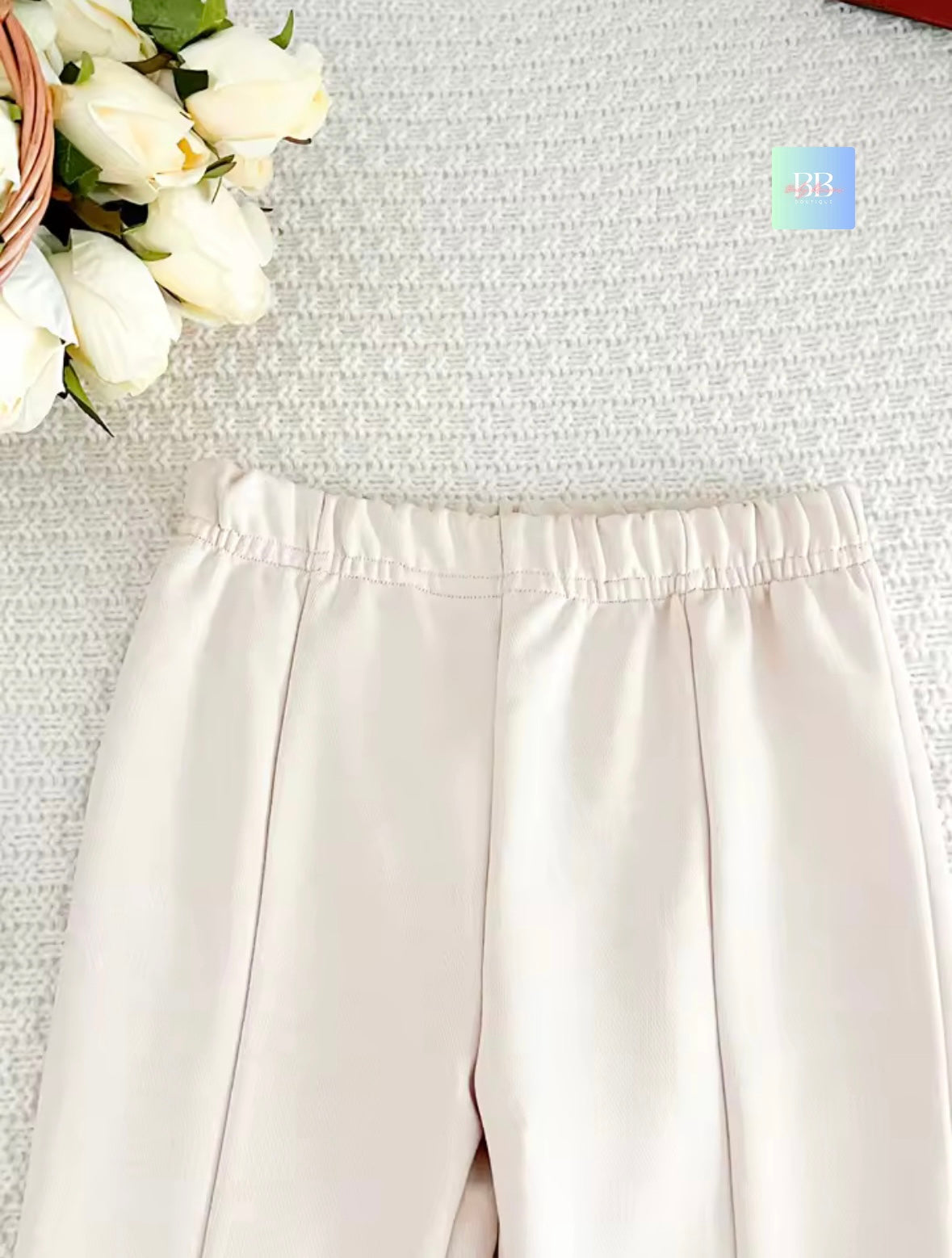 Beige pants on a textured surface with white flowers in the corner
