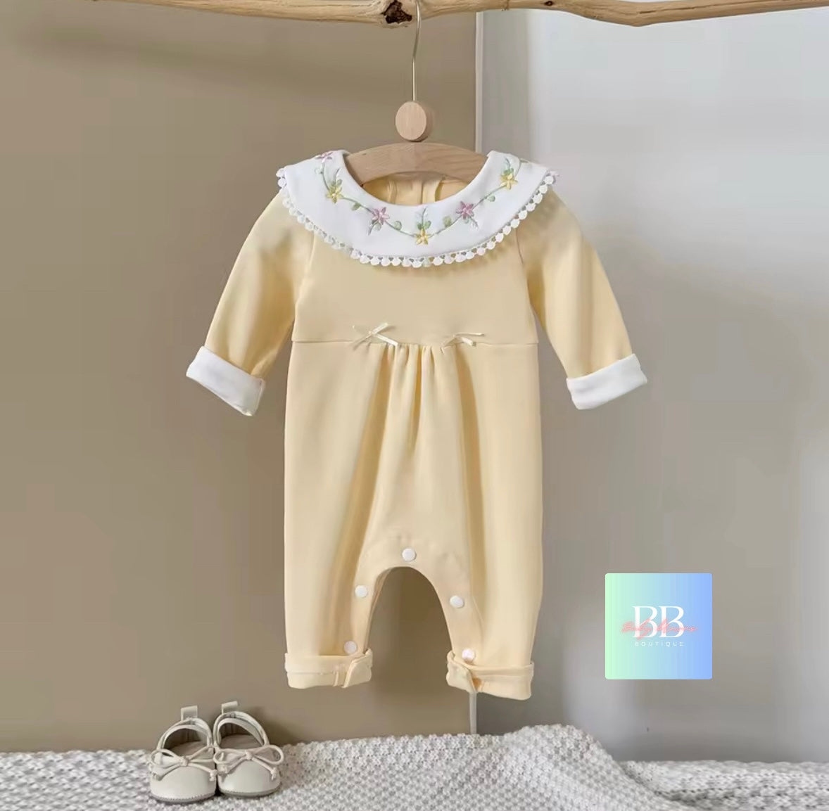 Baby romper with floral collar hanging on a wooden hanger against a neutral wall.