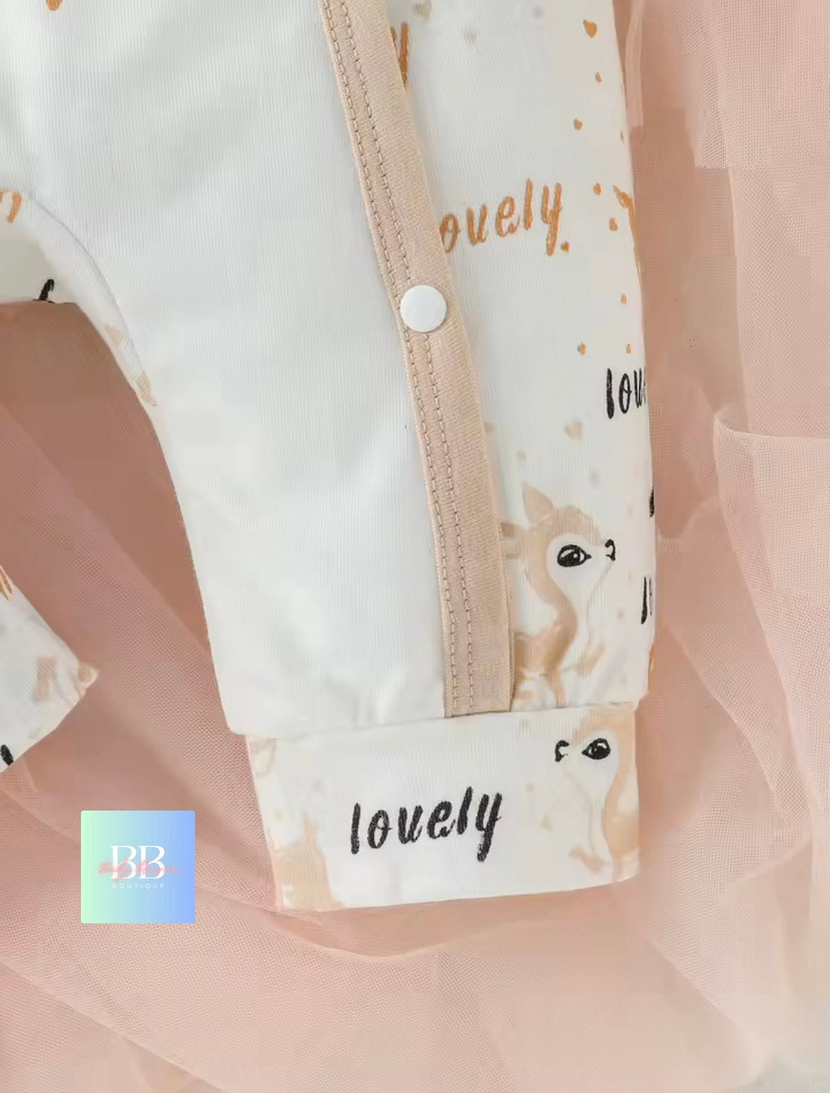 Close-up of a baby outfit with 'lovely' text and animal illustrations on a soft pink background.