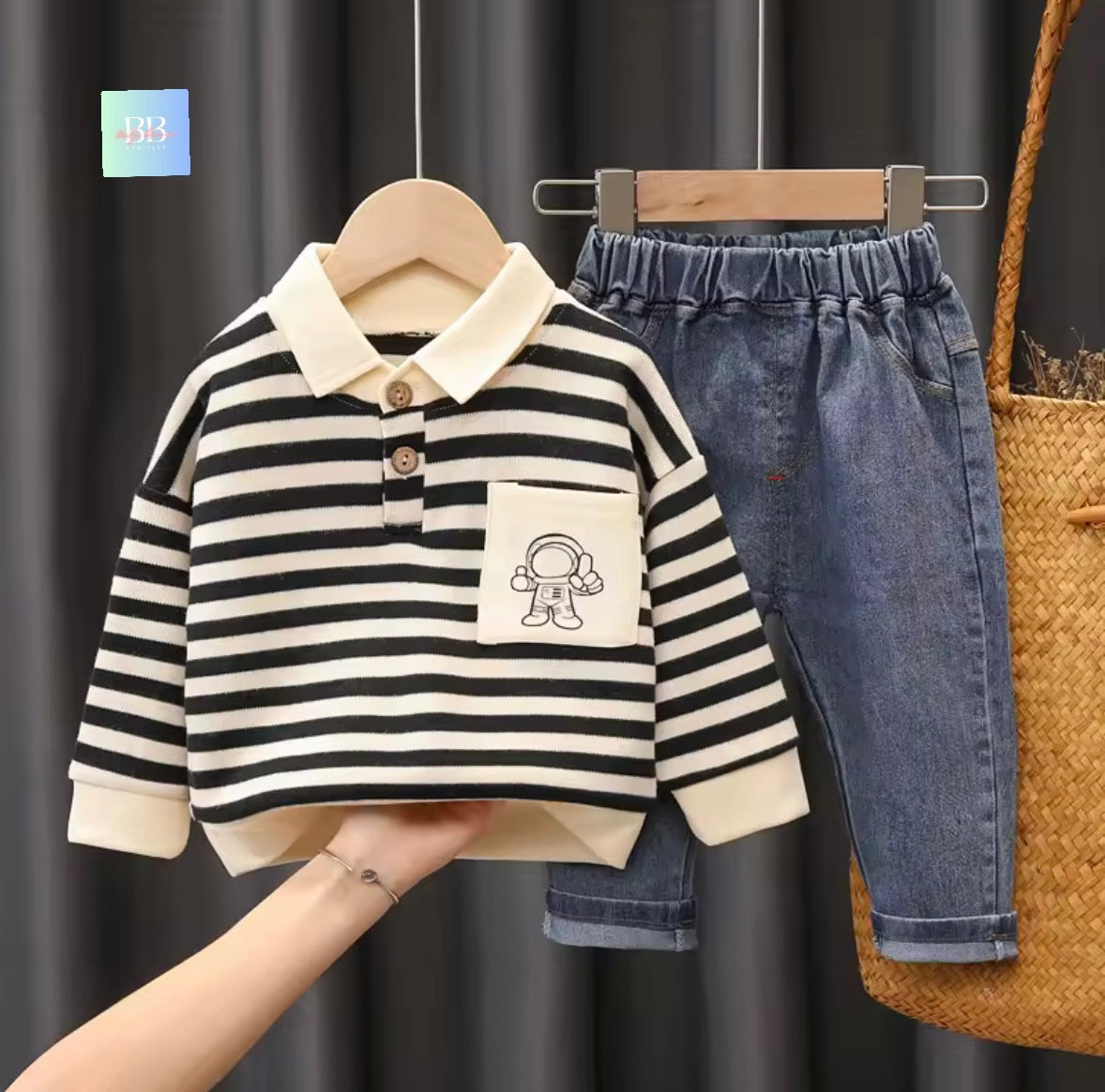 Black and white striped shirt with a small design on a hanger against a dark curtain background.