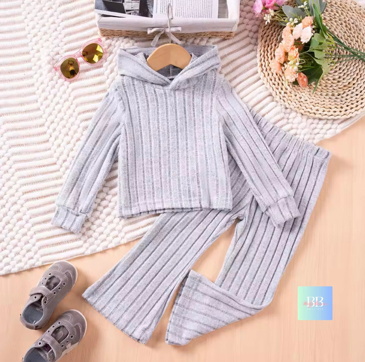 Gray ribbed sweater and pants set on a wooden surface with a woven mat and decorative items.
