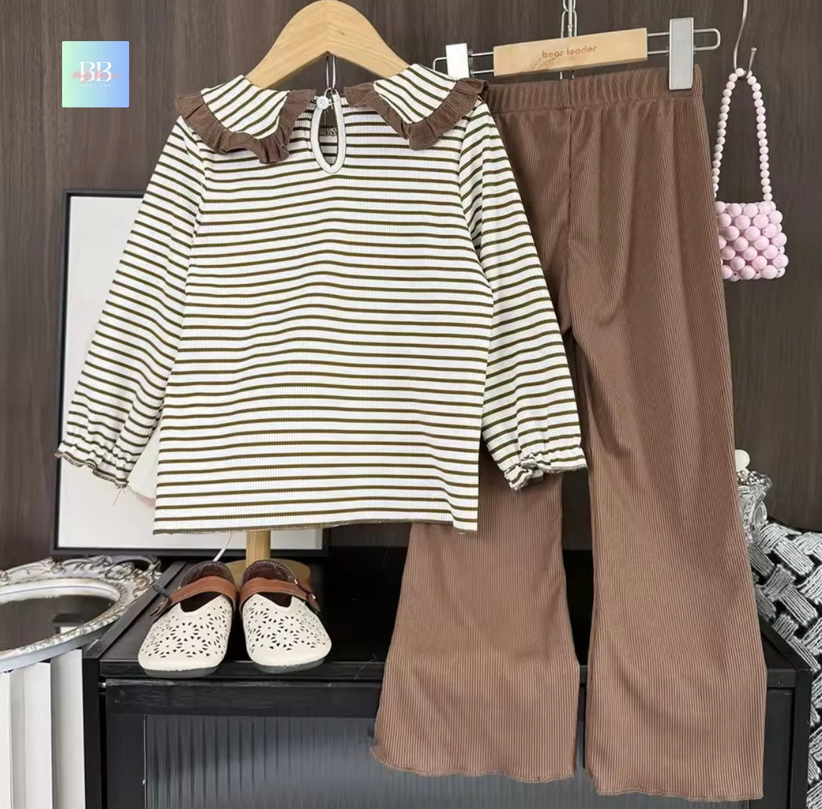 Striped shirt and brown pants on hangers with a handbag in the background.
