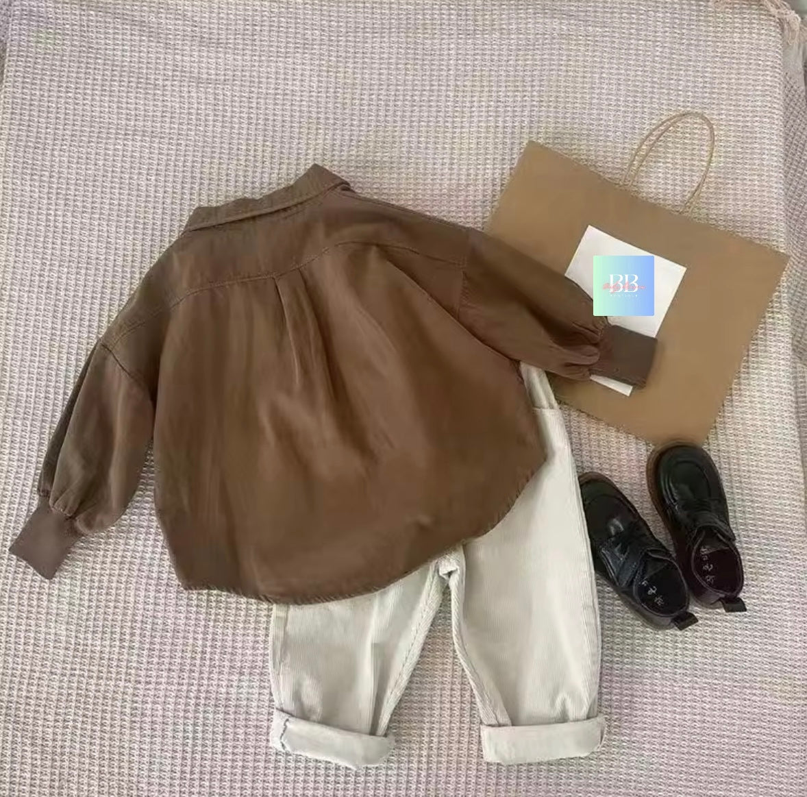 Brown jacket, white pants, black shoes, and a brown bag on a textured surface