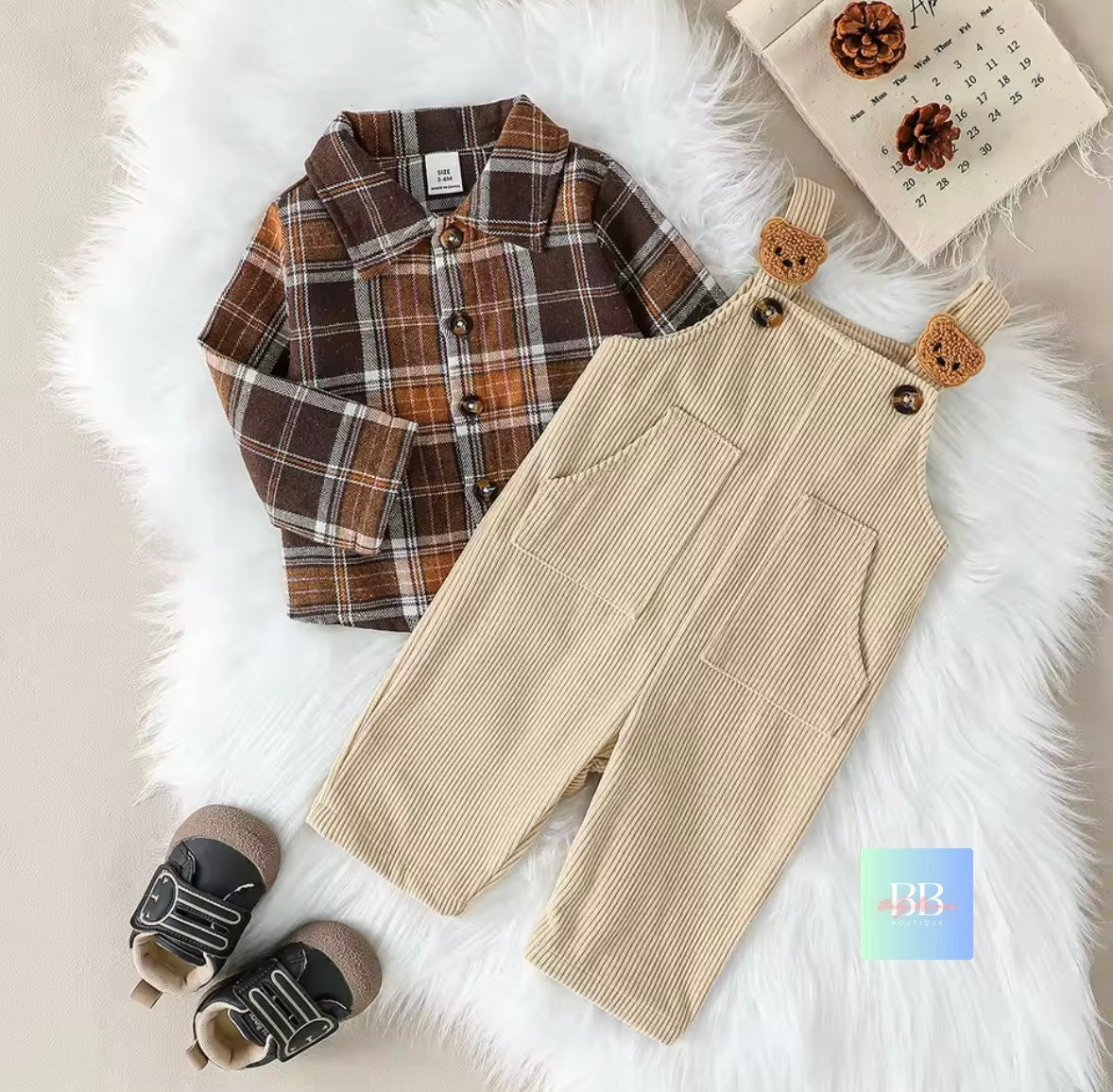 Children's plaid shirt, beige overalls with bear ears, and shoes on a fluffy white surface.