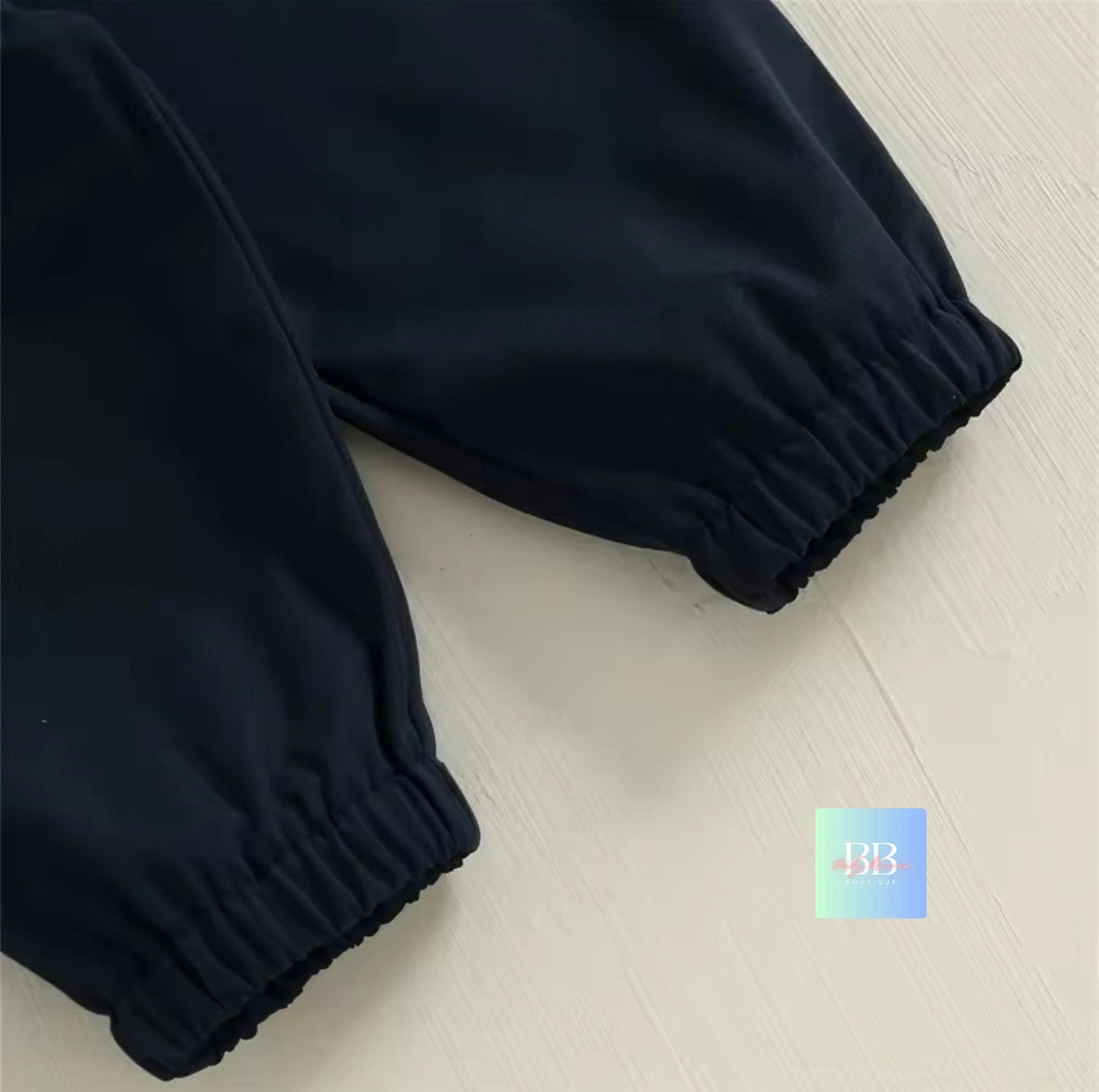 Black pants on a light wooden floor with a brand logo in the corner.