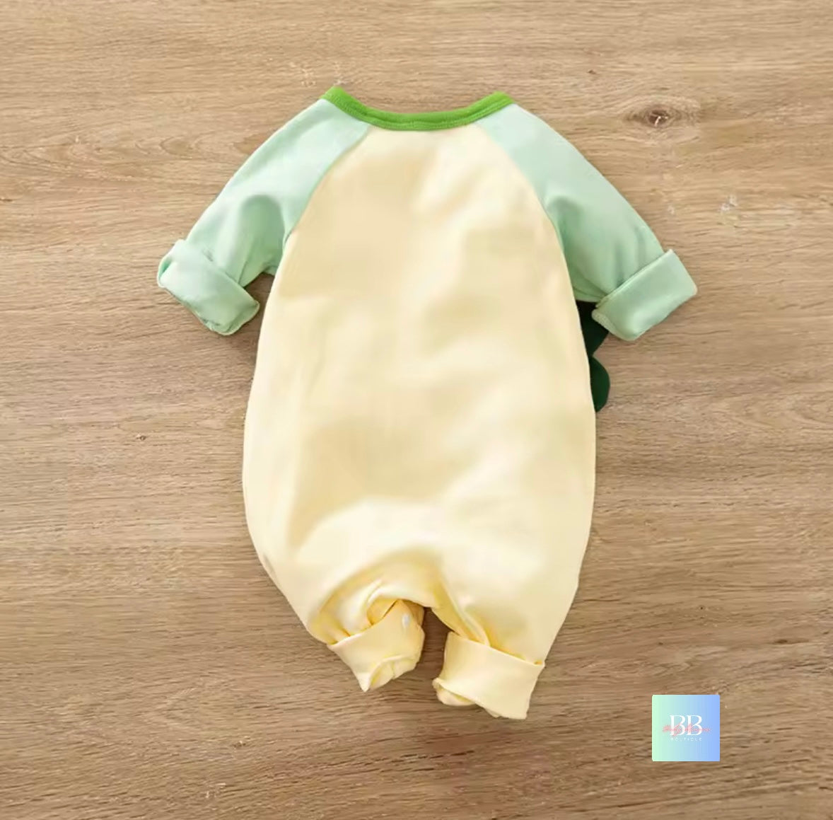 Baby romper with green sleeves on a wooden surface