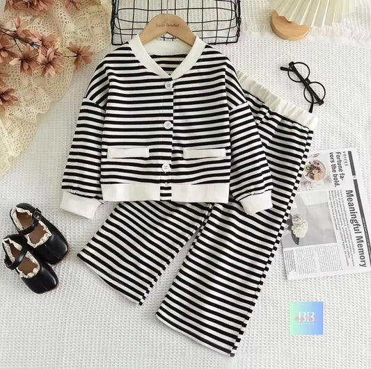 Black and white striped children's outfit on a hanger with shoes and a newspaper on a light surface.