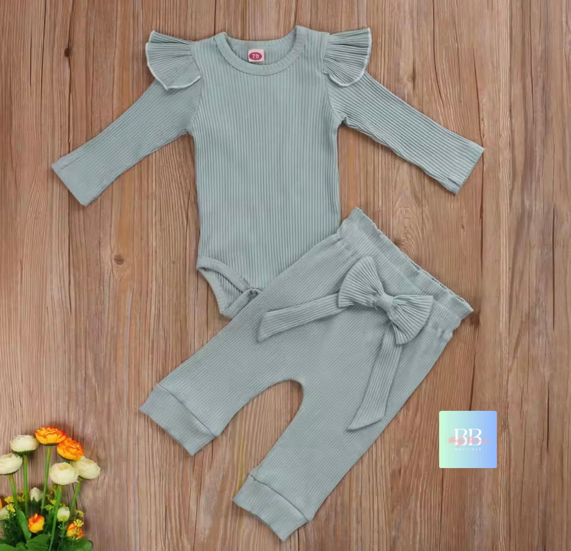 Gray baby outfit with ruffled long-sleeve top and bow-legged pants on a wooden surface.