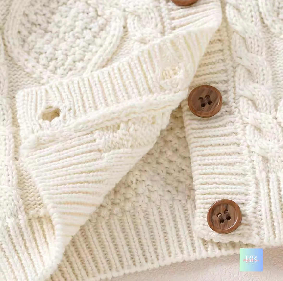 Close-up of a cream-colored knitted cardigan with brown buttons on a neutral background