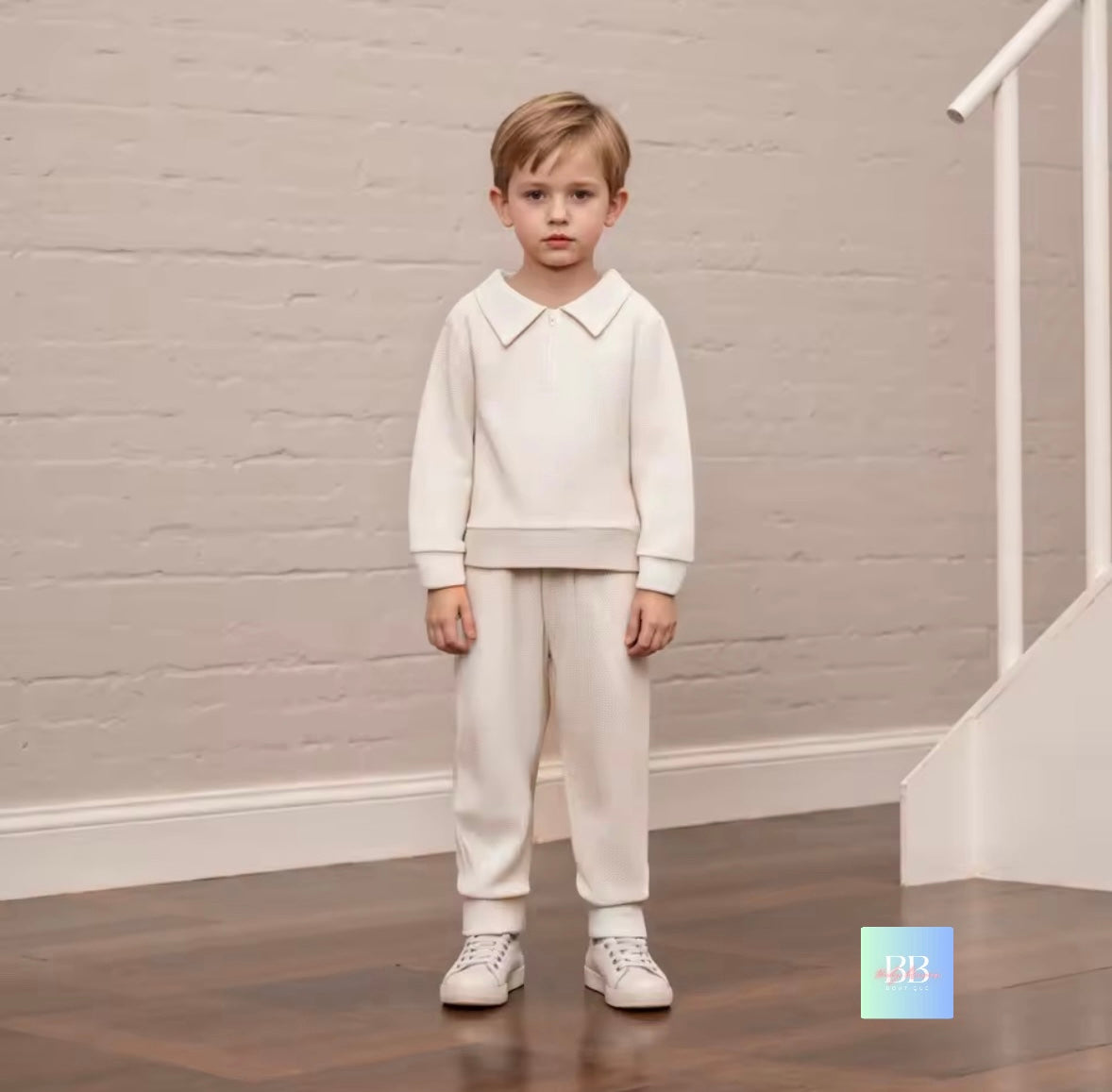 Young boy in a white outfit standing in a room with a neutral background