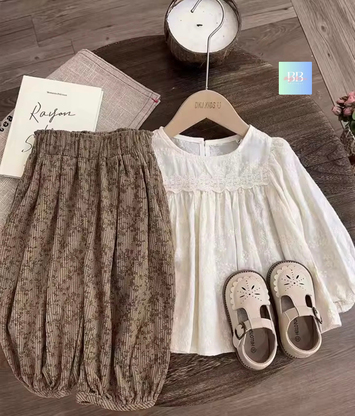 Children's outfit with white top, brown pants, and shoes on a wooden floor.