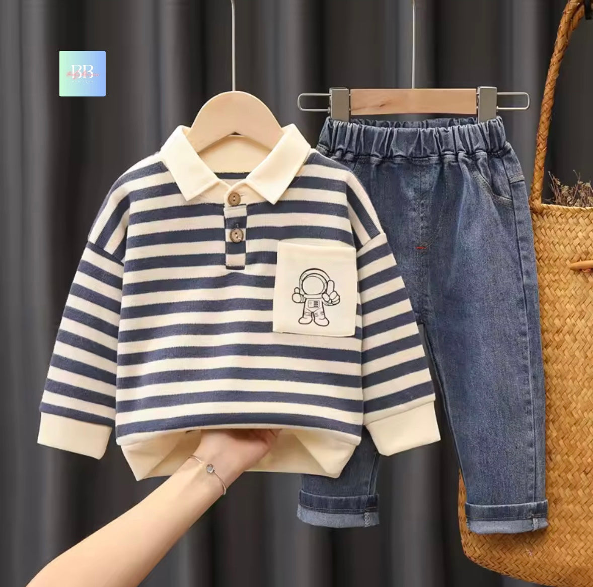 Children's striped shirt with a pocket featuring an astronaut design, paired with blue jeans, against a dark curtain background.