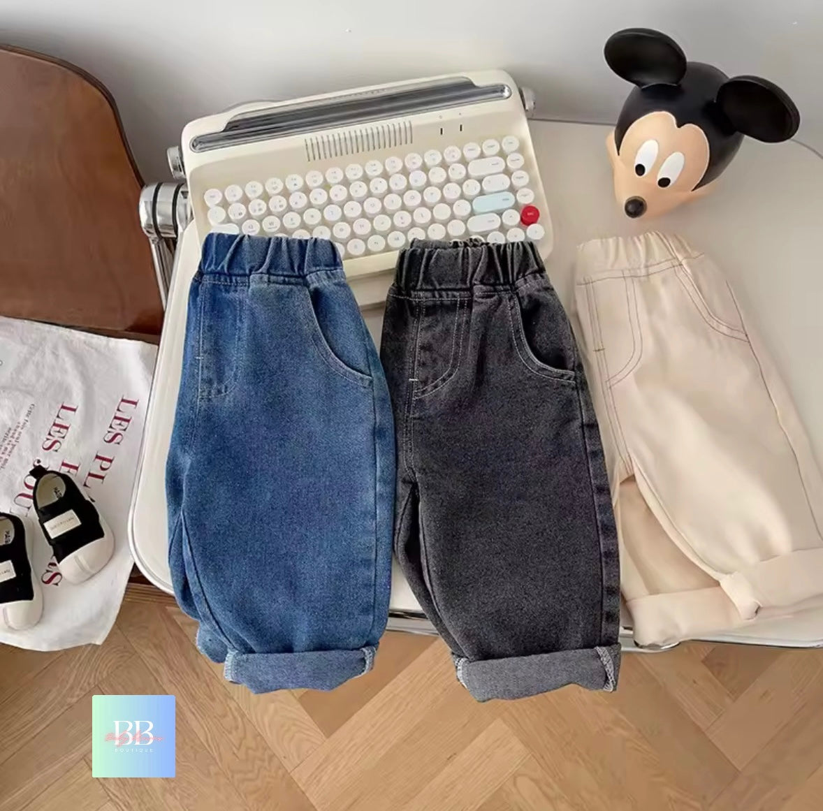 Two pairs of children's jeans on a desk with a typewriter and a toy mouse.