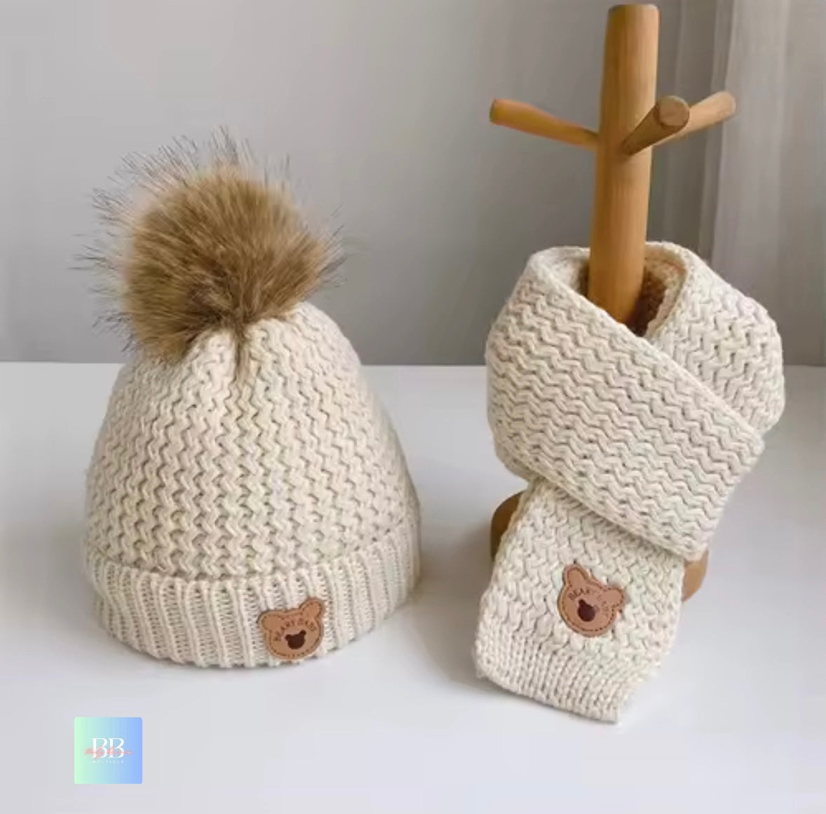 Knitted beige hat and scarf set with bear emblem on a white surface