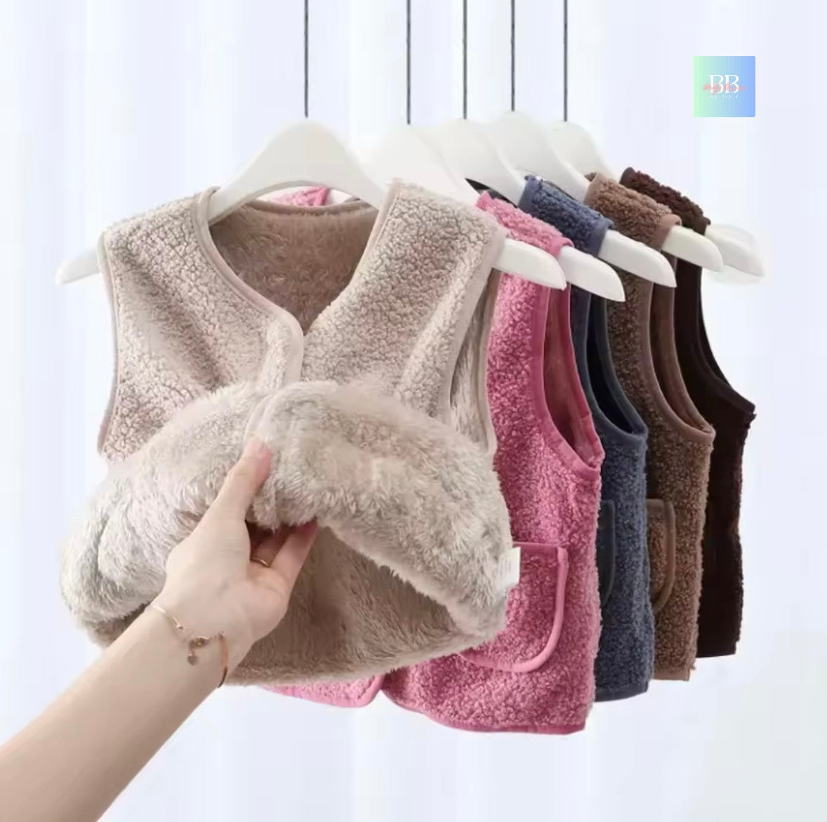 Row of colorful vests on hangers with a hand holding one vest.