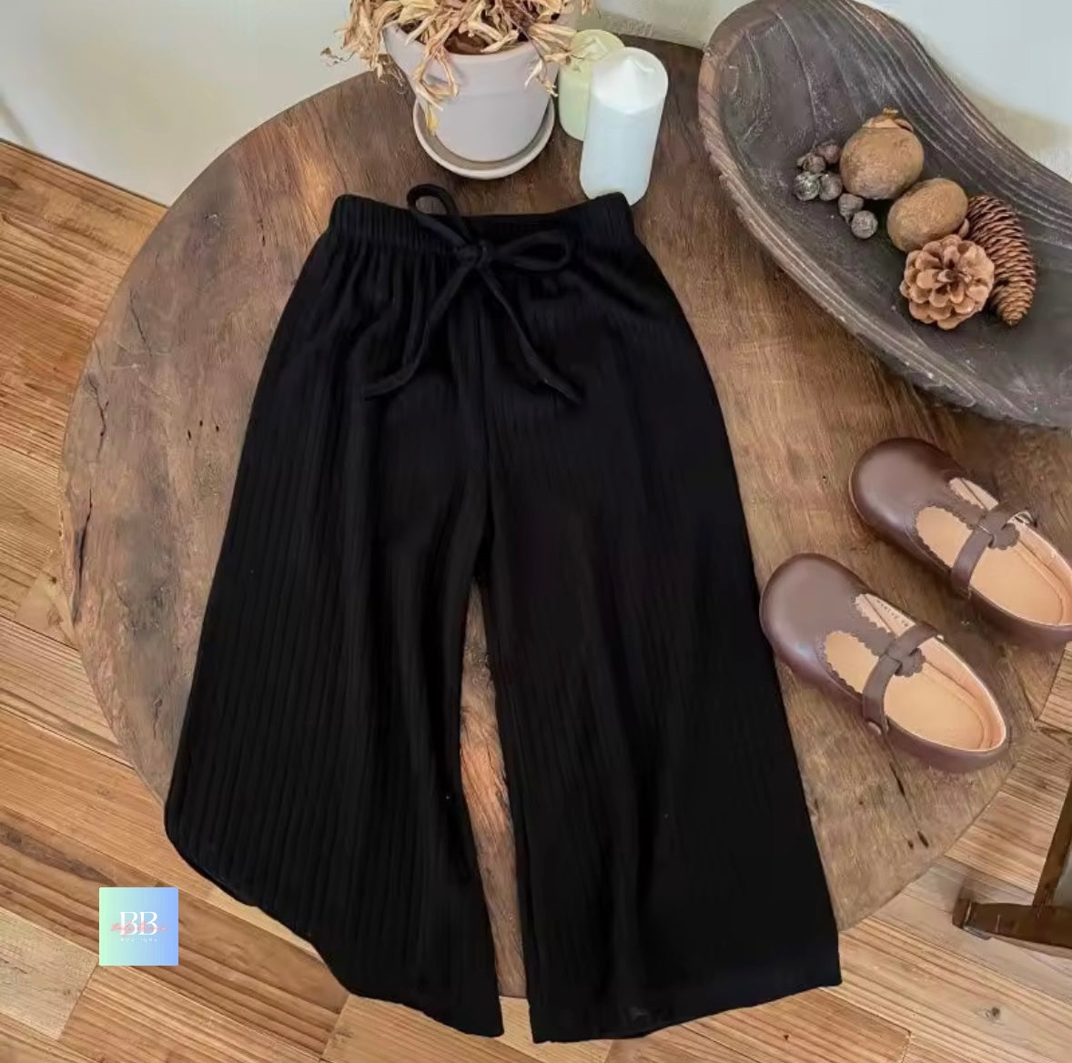 Black pants on a wooden table with shoes and decor items.