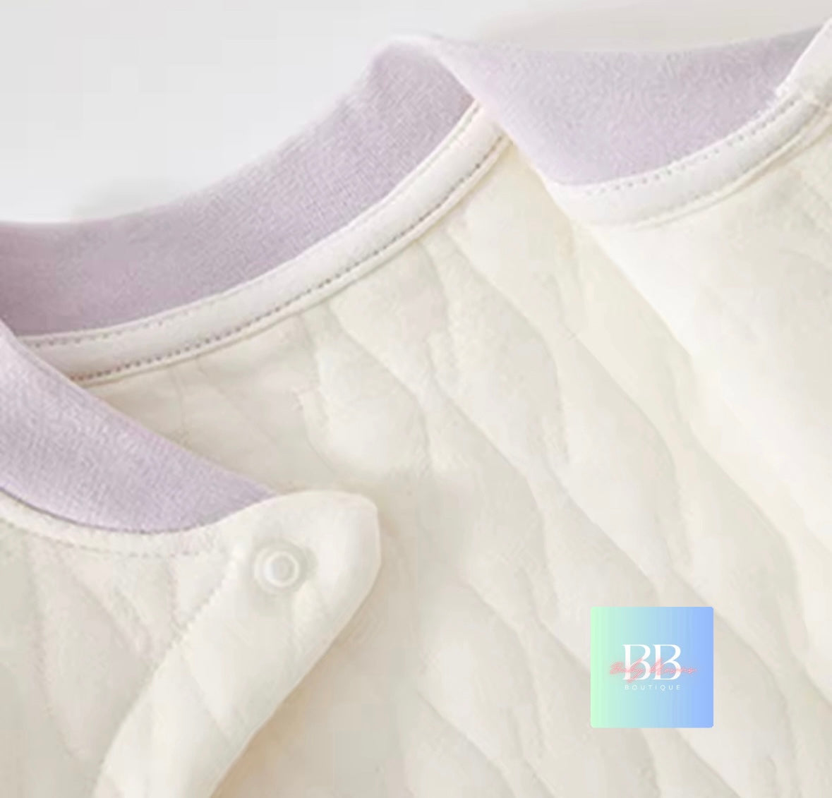 Close-up of a white baby outfit with a collar and button, featuring a brand logo in the corner.