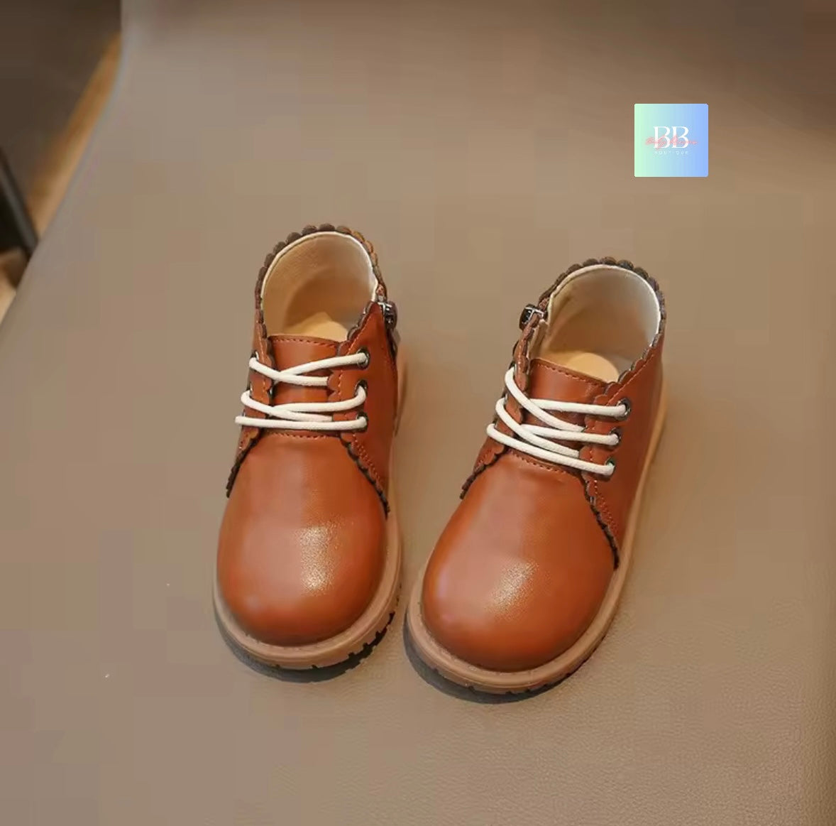 Pair of brown leather boots with white laces on a beige surface