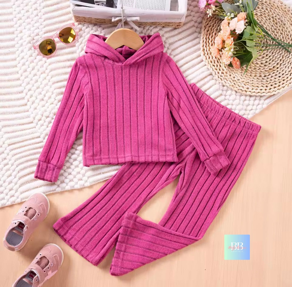 Pink ribbed sweater and pants set on a textured surface with shoes and flowers.