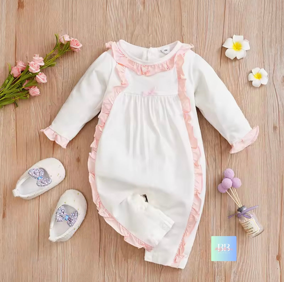 Baby romper with pink trim on a wooden surface with decorative items.